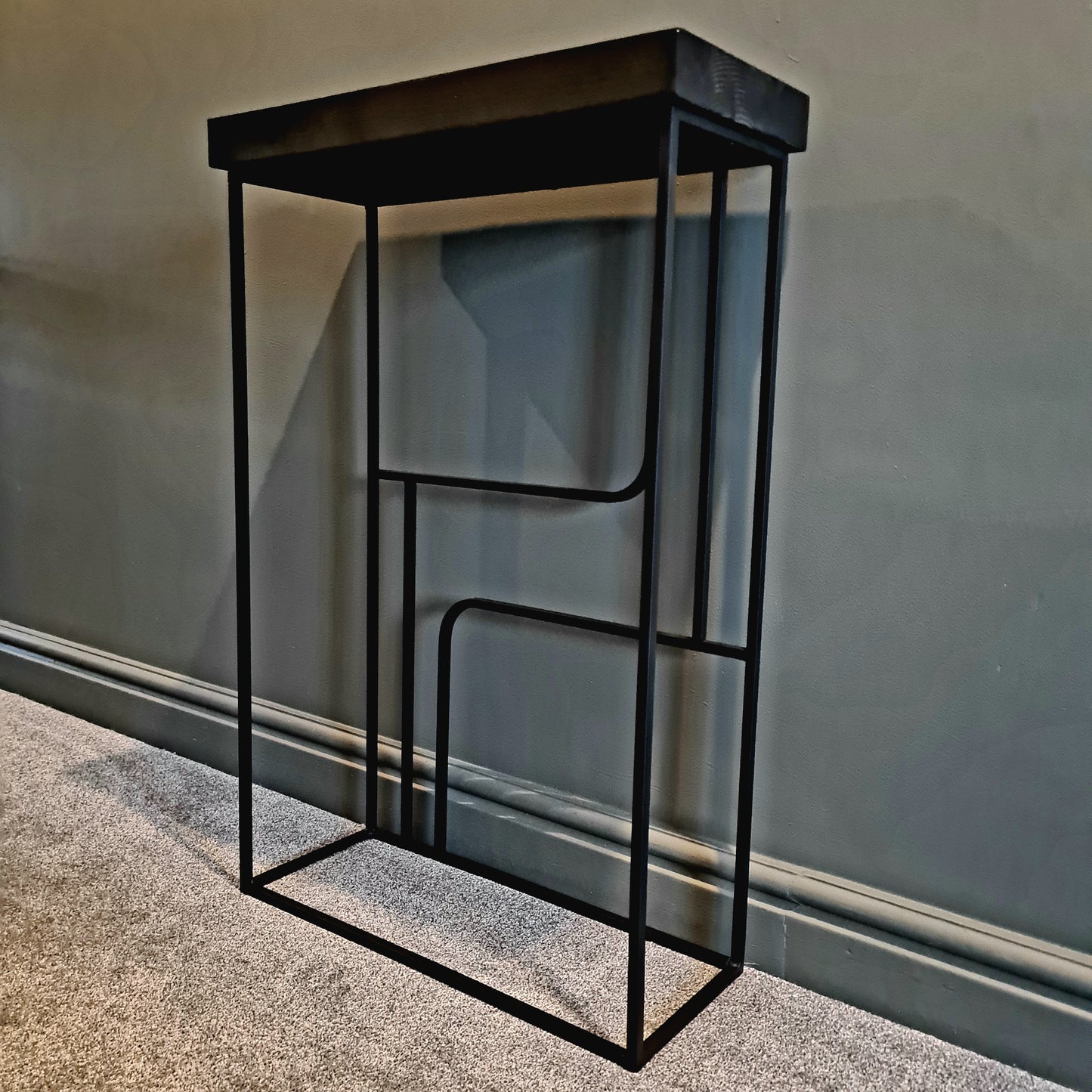 Black metal side table against a gray wall