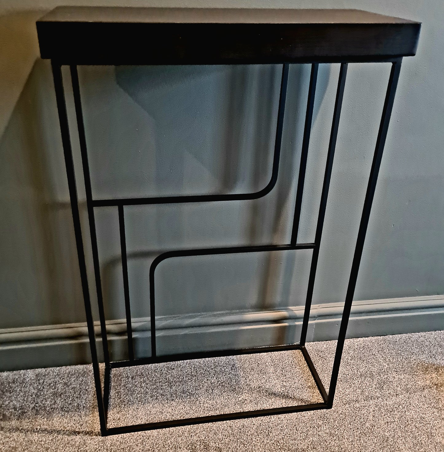 Small black metal table with a wooden top on a carpeted floor.