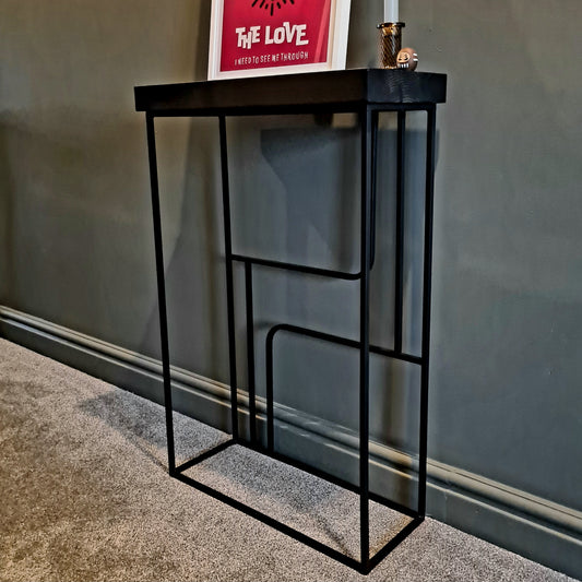 Black metal console table against a gray wall with a framed picture on top.